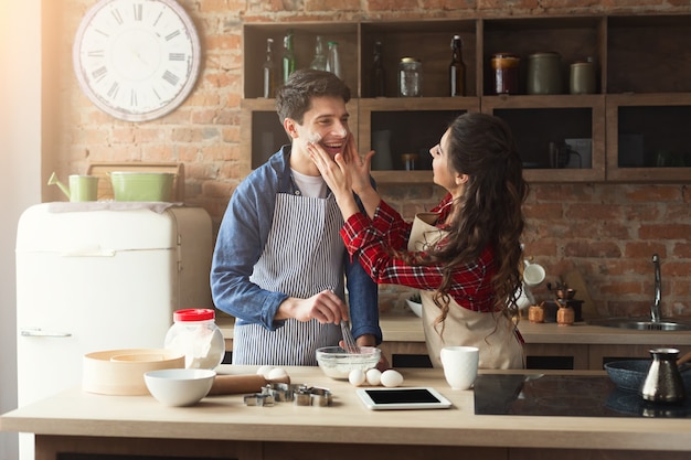 Счастливая молодая женщина и мужчина, выпекающий пирог и весело проводящий время на кухне-чердаке. Молодая семья готовит дома, используя цифровой планшет. Мокап рецепта