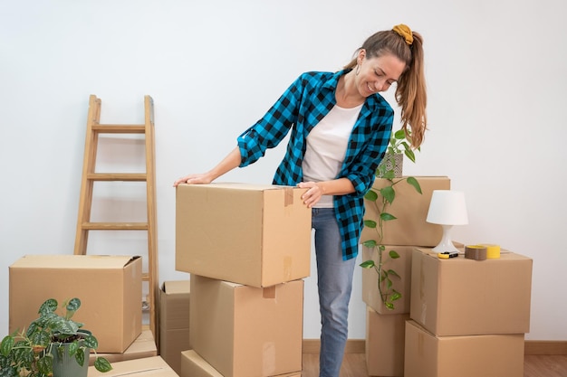 Happy young woman moving in to new home surrounded with cardboard boxes