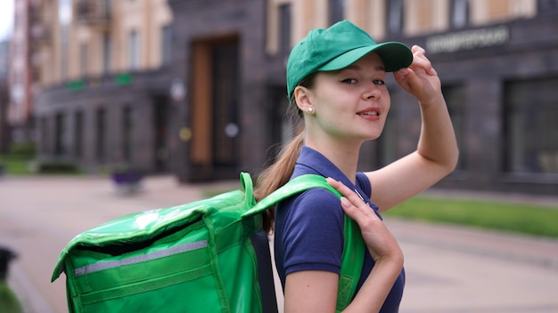 Фото Счастливая молодая женщина или девушка-подросток курьер в зеленой форме с большой термо сумкой или рюкзаком доставки