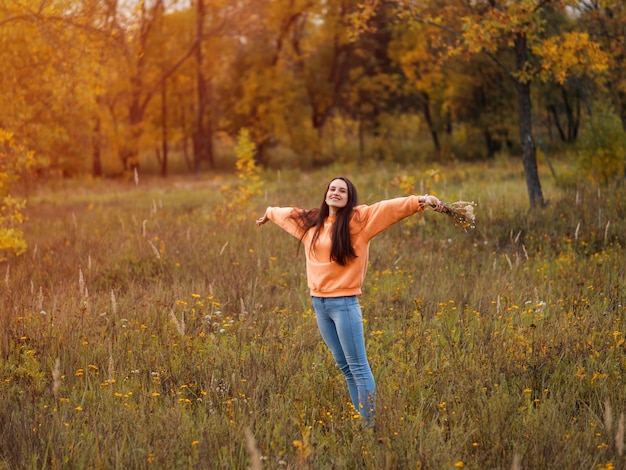 Happy young woman in orange hoodie walking in autumn forest . Lifestyle