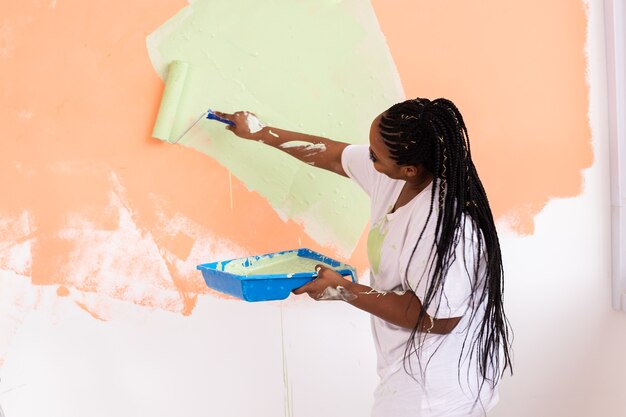 Happy young woman paints the wall with paint