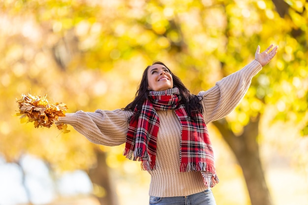 A happy young woman in a park throws leaves during an Indian summer and enjoys autumn