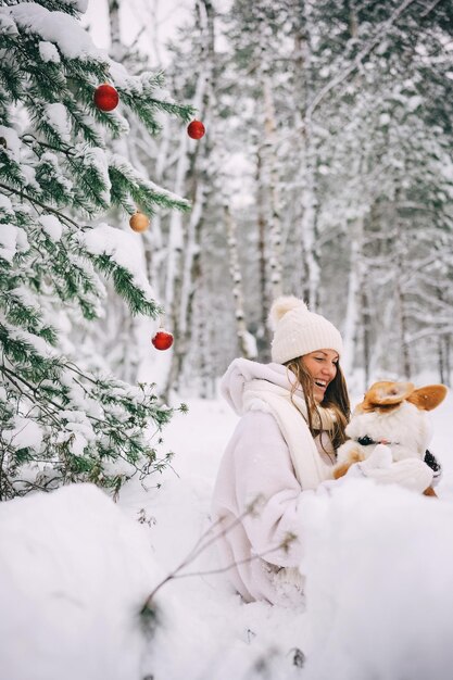 Happy young woman playing with her welsh corgi pembroke puppy in winter forest