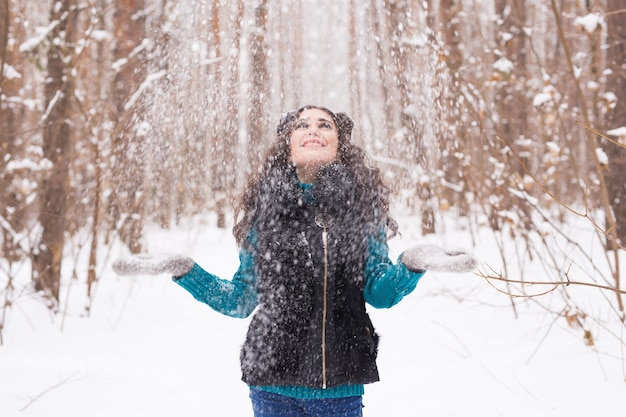 幸せな若い女性は屋外の雪に覆われた森で雪と遊ぶ