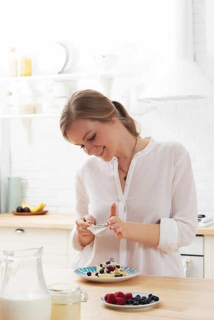 Happy young woman preparing tasty snacks at the kitchen table in the morning light