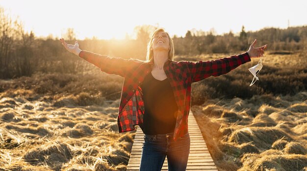 Happy young woman raising hands with a removed knN95 FFP2 protective mask and spending time on vacation during exploring the nature at corona pandemic