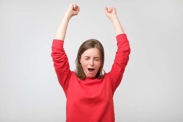 Happy young woman in red wear gesturing and keeping eyes closed