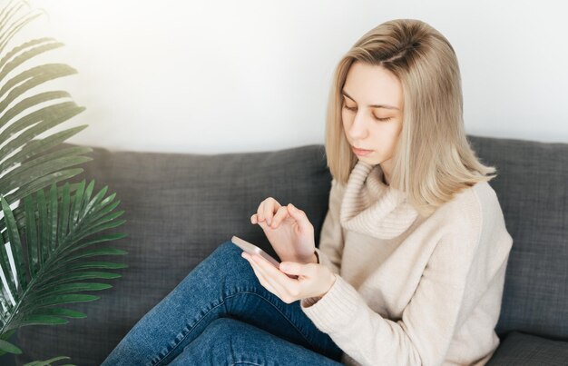 Happy young woman relaxing on comfortable couch holding smartphone in hands