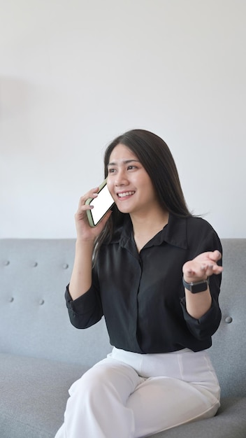 Happy young woman resting on couch at home and talking on cellphone