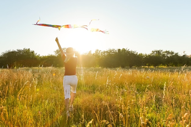 夏の日没時に空き地に凧と一緒に走っている幸せな若い女性