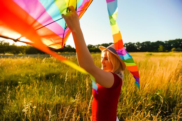 夏の日没時に空き地に凧と一緒に走っている幸せな若い女性