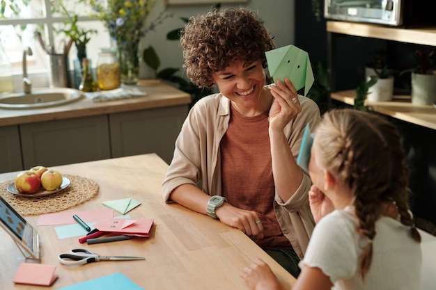 Photo happy young woman showing her youthful daughter green paper origami