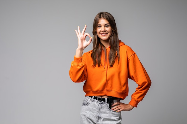 Happy young woman showing ok sign with fingers an winking on a gray