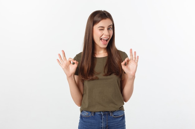 Happy young woman showing ok sign with fingers an winking isolated on a gray background.