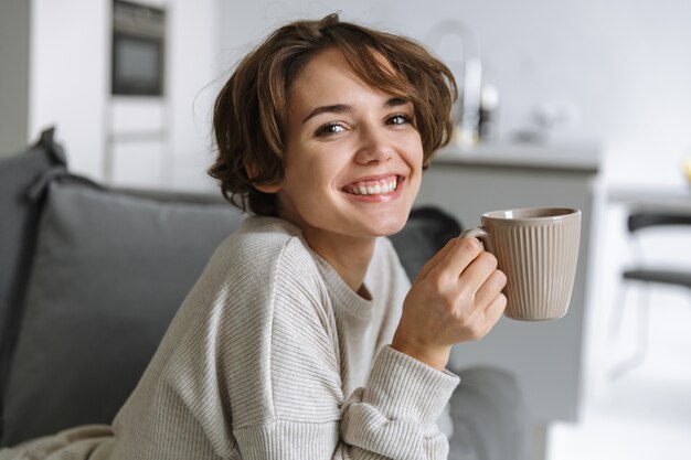 Happy young woman sitting on a couch at home, holding mug