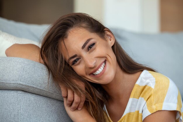 Happy young woman sitting on sofa at home and looking at camera Portrait of beautiful woman smiling and relaxing during summer