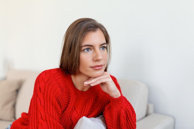 Happy young woman sitting on sofa at home and looking at camera Portrait of comfortable woman in winter clothes relaxing on armchair Portrait of beautiful woman smiling and relaxing during autumn