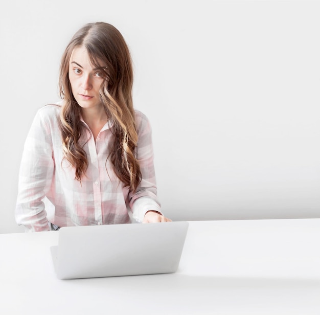 Happy young woman sitting at the table and using a laptop on a gray background