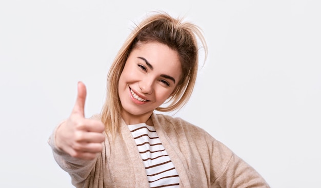 Happy young woman smiling cheerfully and making thumb up sign showing her support and respect to someone or something Pretty Caucasian female making positive gesture Body language Good job