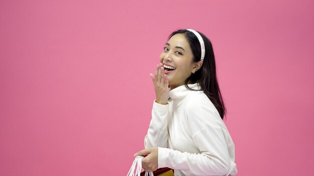 Happy young woman smiling and hold shopping bags and credit card while doing some shopping on a pink studio background person