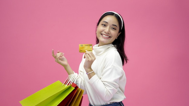 Felice giovane donna sorridente e tenere borse della spesa e carta di credito mentre fa un po' di shopping su uno sfondo rosa studio