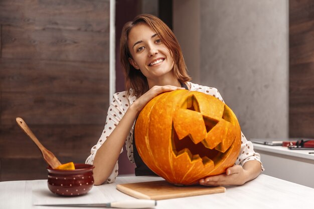 ハロウィーンを祝っている間、笑顔でジャックのカボチャのランタンを抱き締めて幸せな若い女性