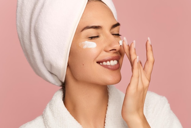 happy young woman smiling while applying facial cream after shower