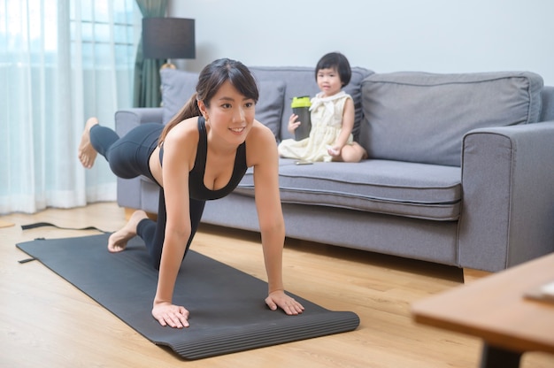Счастливая молодая женщина в спортивной одежде с дочерью тренируется в гостиной дома