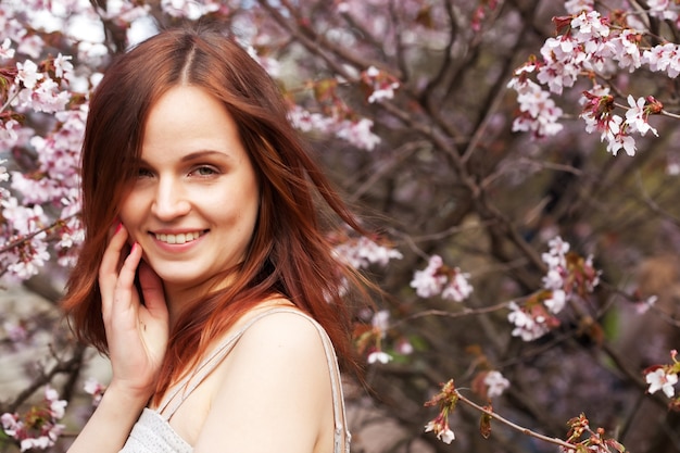 Happy young woman in spring flowers garden lifestyle portrait. Sakura garden.