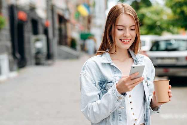 幸せな若い女立っていると屋外の画面を見てスマートフォンを保持