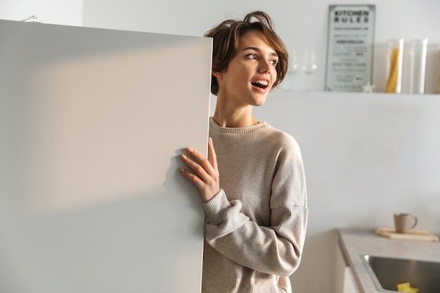 Happy young woman standing at the opened fridge