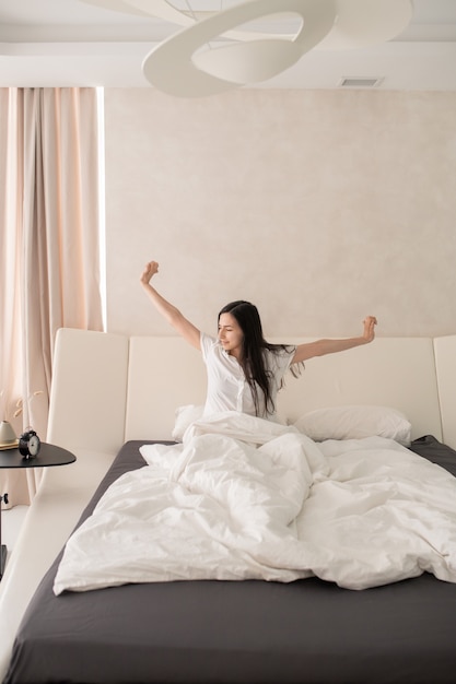 Happy young woman stretching arms in bed after sleep