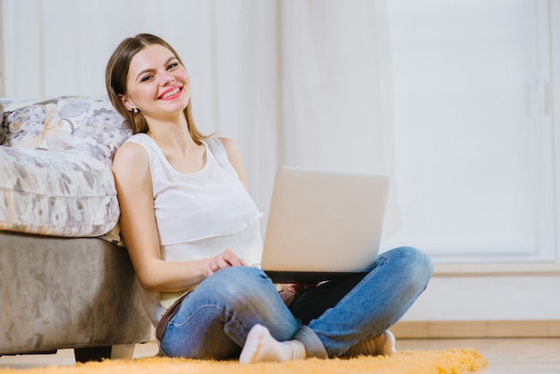 Happy young woman or student with laptop sitting on the floor at home