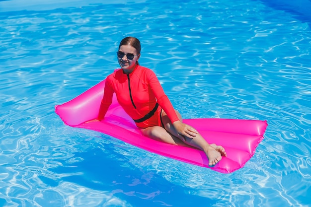 Happy young woman in sunglasses and pink bikini floating on inflatable mattress by the pool Summer vacation concept Travel by sea