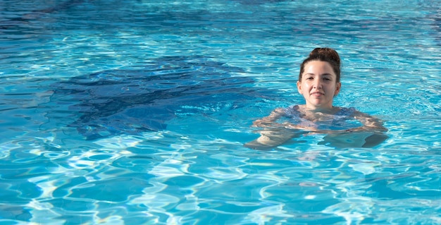 Felice giovane donna nuota in piscina sotto il sole.