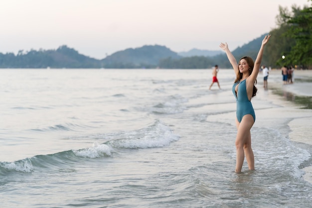 Happy young woman in swimsuit with arms raised on the sea beach at Koh Chang island Thailand