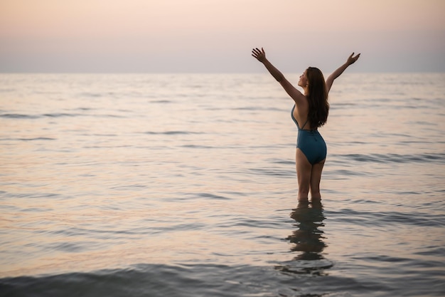 Happy young woman in swimsuit with arms raised on the sea beach at Koh Chang island Thailand