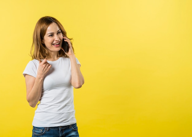 Giovane donna felice che parla sul telefono cellulare contro fondo giallo