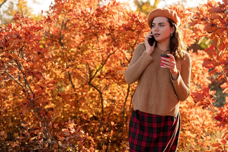 Photo happy young woman talking on mobile phone in autumn park with red foliage on background autumn mood concept copy space