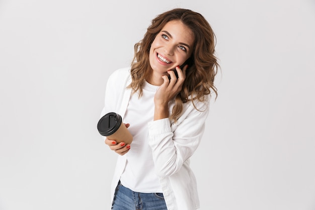 Happy young woman talking on mobile phone and drinking takeaway coffee isolated