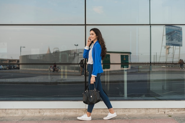 Happy young woman talking on the phone and walking