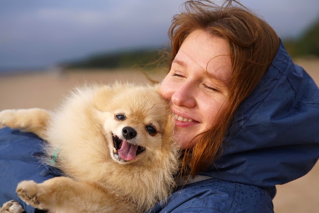 Foto una giovane donna felice o un'adolescente che cammina con il suo cane pomeranian spitz sulla spiaggia tiene un cucciolo