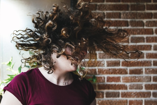 Foto una giovane donna felice che lancia i capelli contro il muro.