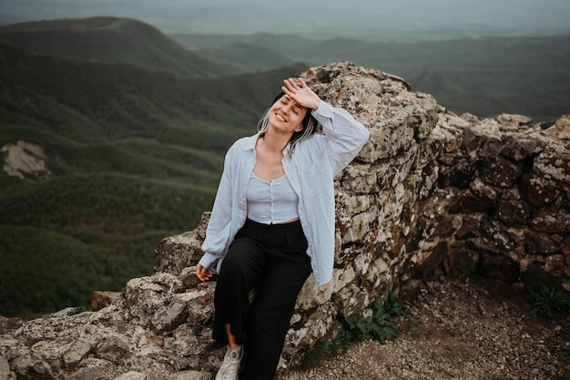 Happy young woman tourist hiking up on top of mountain enjoying nature landscape in cloudy gloomy