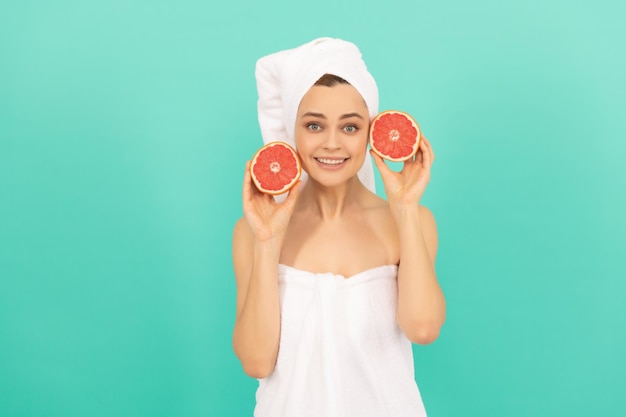 Happy young woman in towel after shower with grapefruit on blue background beauty