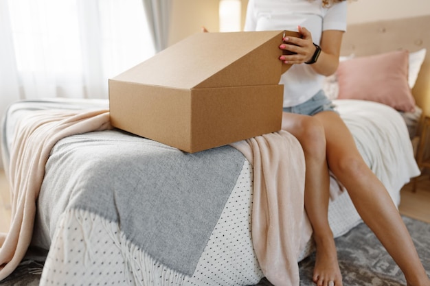 幸せな若い女性が寝室でパッケージを開く