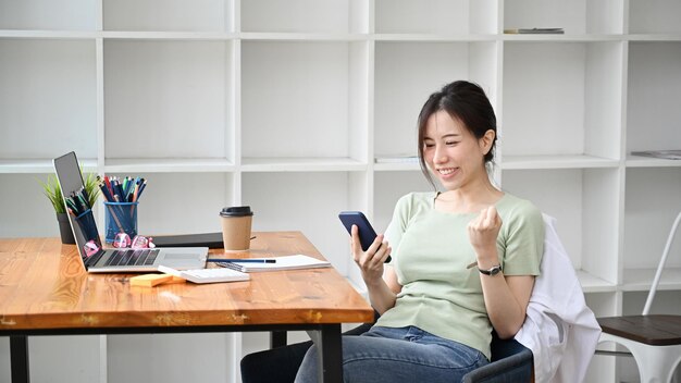 Happy young woman using smartphone and celebrating success