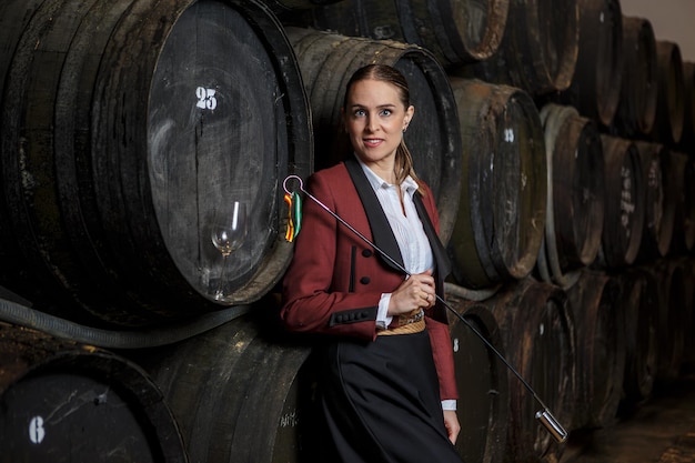Happy young woman venenciador standing near wooden wine barrels with venencia