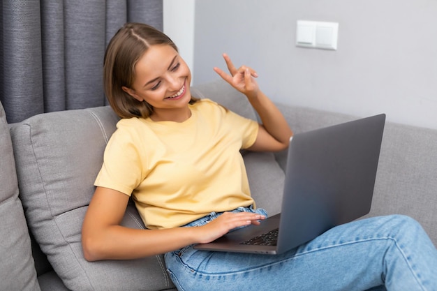 Happy young woman video calling sitting on sofa and using laptop at home