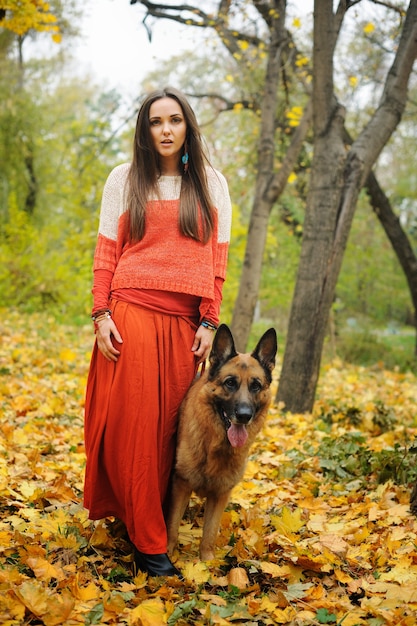 屋外の秋の公園で彼女のジャーマンシェパード犬と一緒に歩く幸せな若い女性